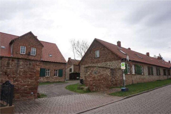 Seitenansicht von Steinbauten mit roten Ziegeldächern an einer Kopfsteinpflasterstraße in Schackensleben