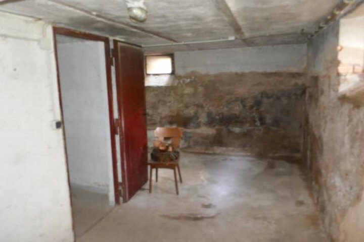 Keller mit Betonboden, verputzten und verputzten Ziegelwänden, roter Tür und einem Holzstuhl im Raum