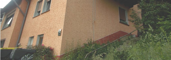 Seitenansicht eines Einfamilienhauses mit orangefarbener Fassade, Fenstern und Vegetation im Vordergrund, Hausnummer 48a in Plettenberg