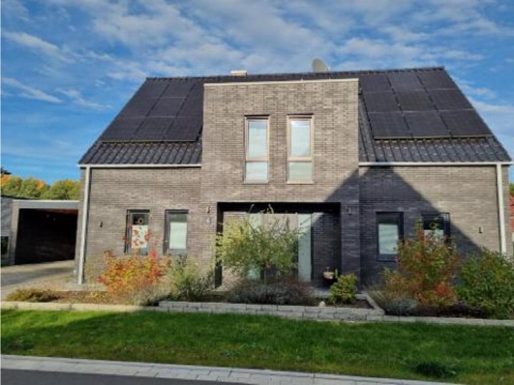 Einfamilienhaus mit grauer Fassade und Solaranlage auf dem Dach, Vorgarten mit Grünflächen und Pflanzen, Eingangsbereich im Zentrum