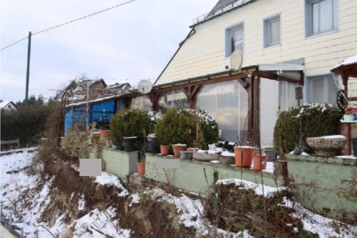 Gartenbereich mit Pflanzen in Töpfen, niedriger Mauer und Schneebedeckung vor einem Haus mit Terrasse in Leienkaul