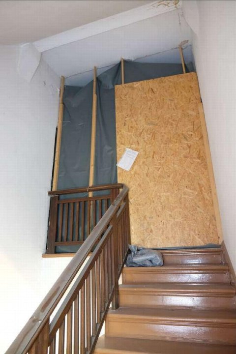 Treppenhaus mit Holztreppe und Geländer, oberer Bereich teilweise mit Sperrholz und Schutzfolie abgedeckt