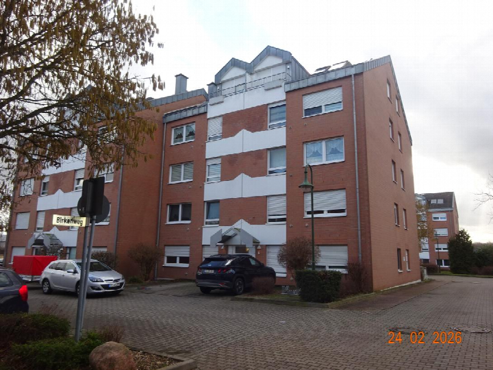 Seitenansicht eines mehrstöckigen Wohngebäudes aus rotem Backstein mit weißen Fassadenelementen und Fenstern, geparkte Autos im Vordergrund, Straßenschild Birkenweg sichtbar