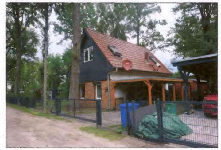 Einfamilienhaus mit Satteldach, dunkler Fassade und Holzveranda, umgeben von Bäumen und einem Zaun, Ansicht von vorne