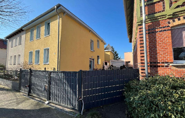 Gelbes Einfamilienhaus an der Karlstraße 5 mit dunklem Zaun und Grünbusch