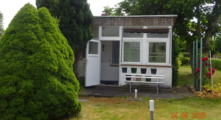 Kleines Haus mit offener Tür, Fenster und Sitzbank im Garten
