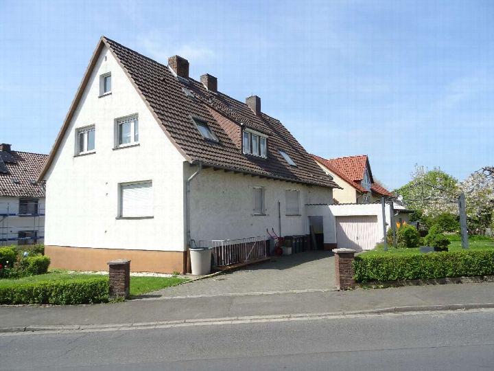 Seitenansicht eines zweifamilienhauses mit braunem Ziegeldach, weißen Wänden und angrenzendem Garten sowie Garage in Guxhagen, Wiesenweg 2