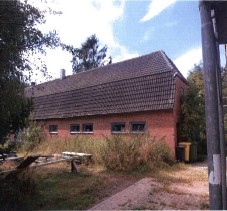 Seitenansicht eines roten Backsteinhauses mit Satteldach und mehreren Fenstern, umgeben von Vegetation, in Bondelum, Oberdorf 16