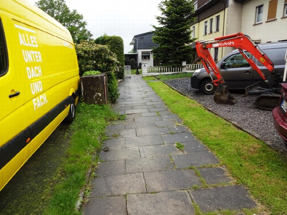Gartenweg aus Pflastersteinen mit Grasbewuchs, gelber Lieferwagen links, roter Mini-Bagger rechts, Wohnhäuser im Hintergrund, Bochum, Zur Wegschere