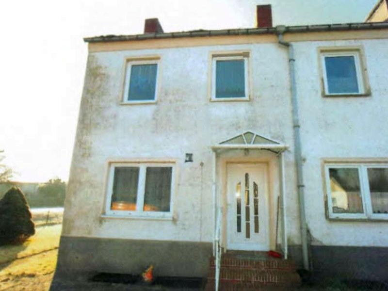Zweistöckiges Reihenhaus in Zemitz, Neubaugebiet 11, mit weißer Fassade, mehreren Fenstern und Eingangstür mit Vordach. Grundstück mit freiem Gelände im Vordergrund