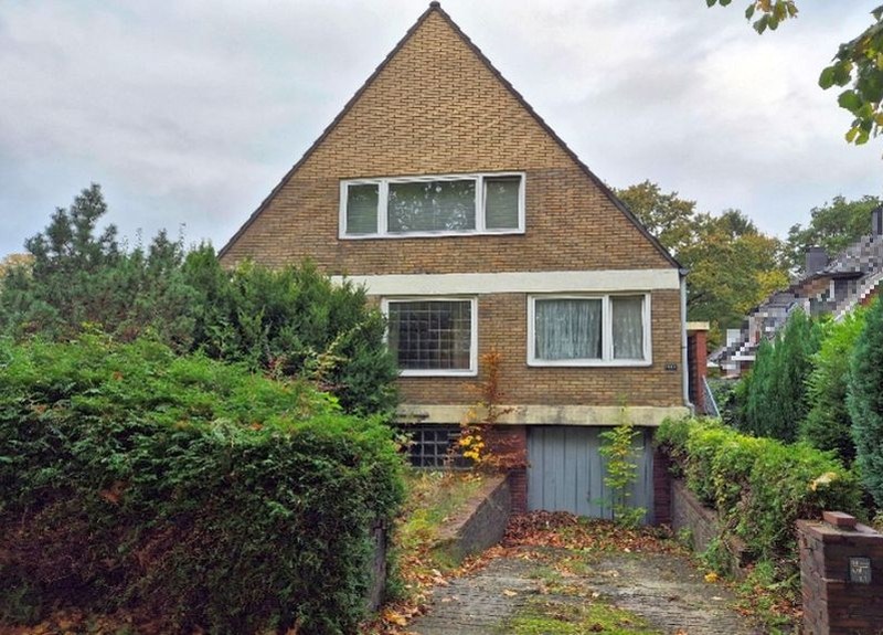 Einfamilienhaus in Hamburg, Pillauer Straße 103, 22047, mit braunem Ziegeldach, Fenstern im Obergeschoss und Einfahrt mit Garagentür, umgeben von Hecken und Laub
