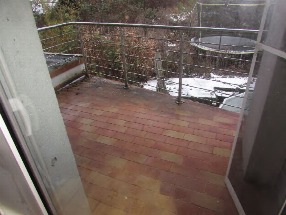 Terrasse mit roten Pflastersteinen und Metallgeländer, im Hintergrund Schnee und Vegetation
