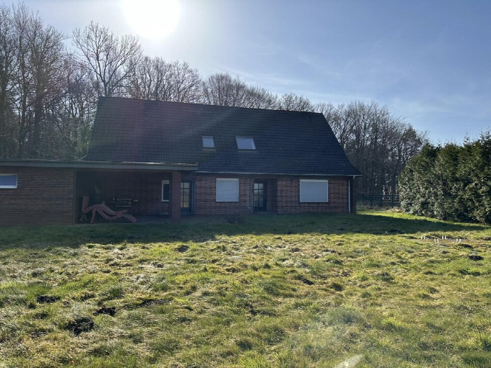 Einfamilienhaus mit Satteldach, Garagenstellplatz und Vorgarten, umgeben von Bäumen und Hecken, bei Tageslicht aufgenommen