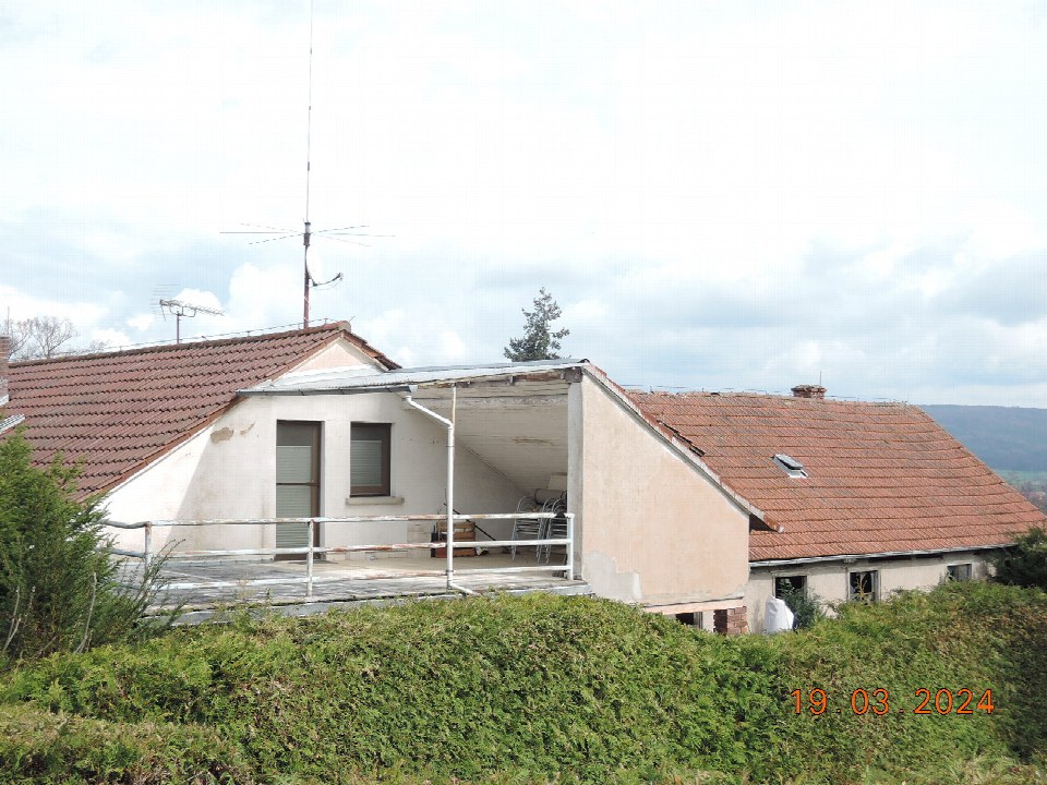 Außenansicht einer Garage mit offener Abstellfläche, Metallgeländer und Dachziegeln, umgeben von Grünanlagen