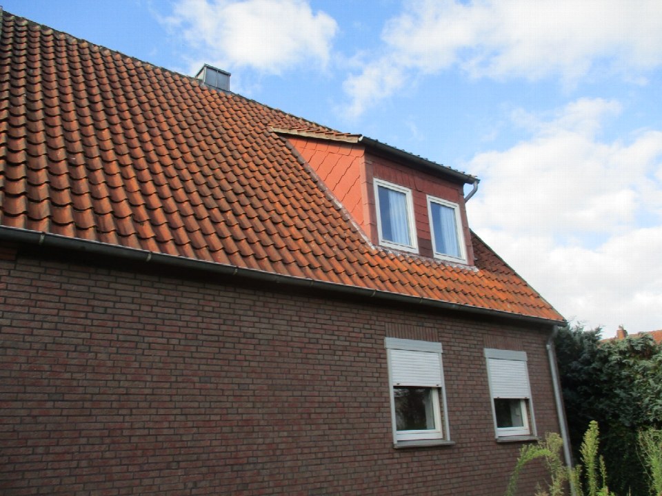 Seitenansicht eines zweifamilienhauses mit rotem Ziegeldach, Dachgaube und Backsteinfassade unter blauem Himmel