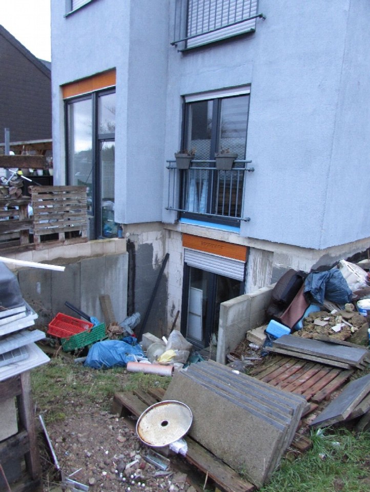Hinterhof eines Doppelhauses mit Baustellenabfällen, Paletten und Gerümpel, teilweise mit Grasbewuchs