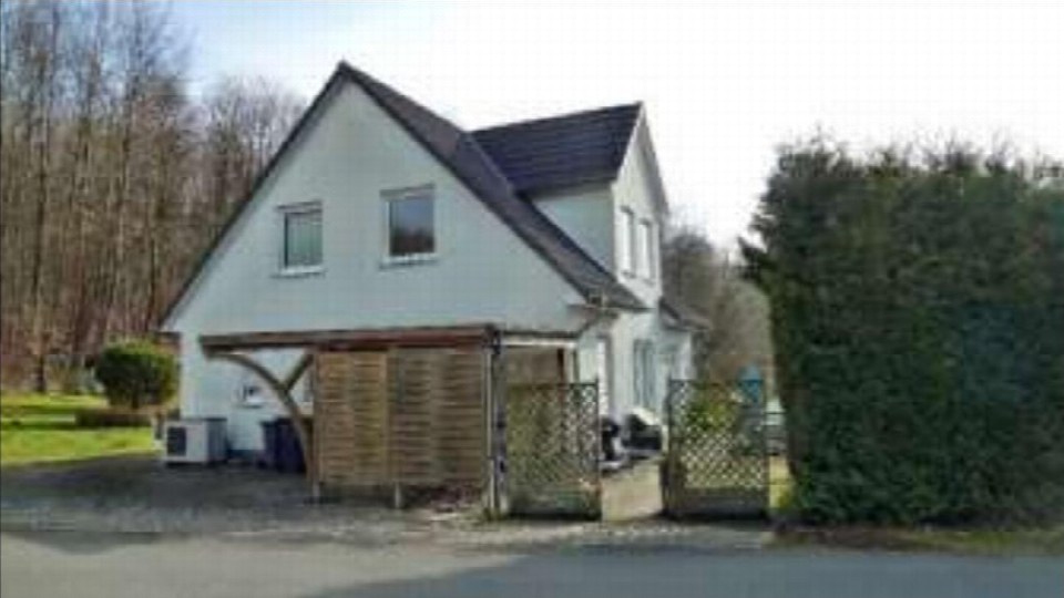 Einfamilienhaus mit weißer Fassade und dunklem Satteldach, Vorgarten und Holzabtrennung vor dem Eingangsbereich