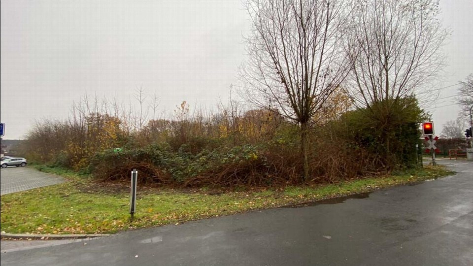 Unbebautes Grundstück mit Grünfläche, Sträuchern und kahlen Bäumen an der Otterstraße in Dinslaken, neben einer Straße und einem Bahnübergang
