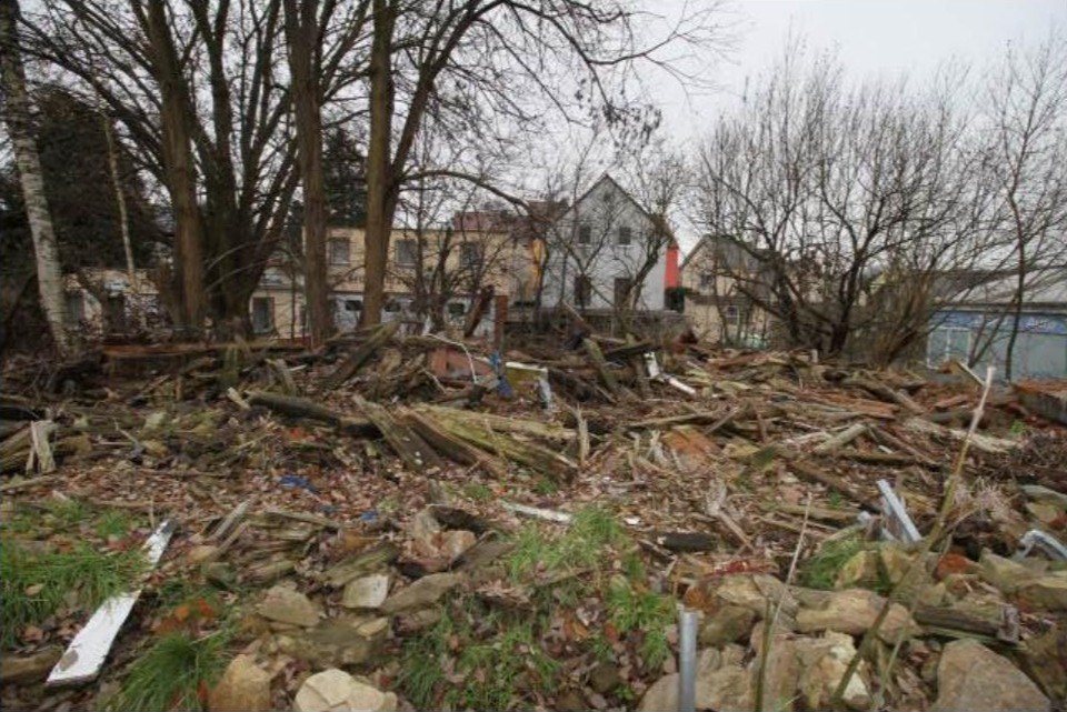 Gartenbereich mit Holztrümmern, Steinen und kahlen Bäumen, im Hintergrund Wohnhäuser in Pulsnitz