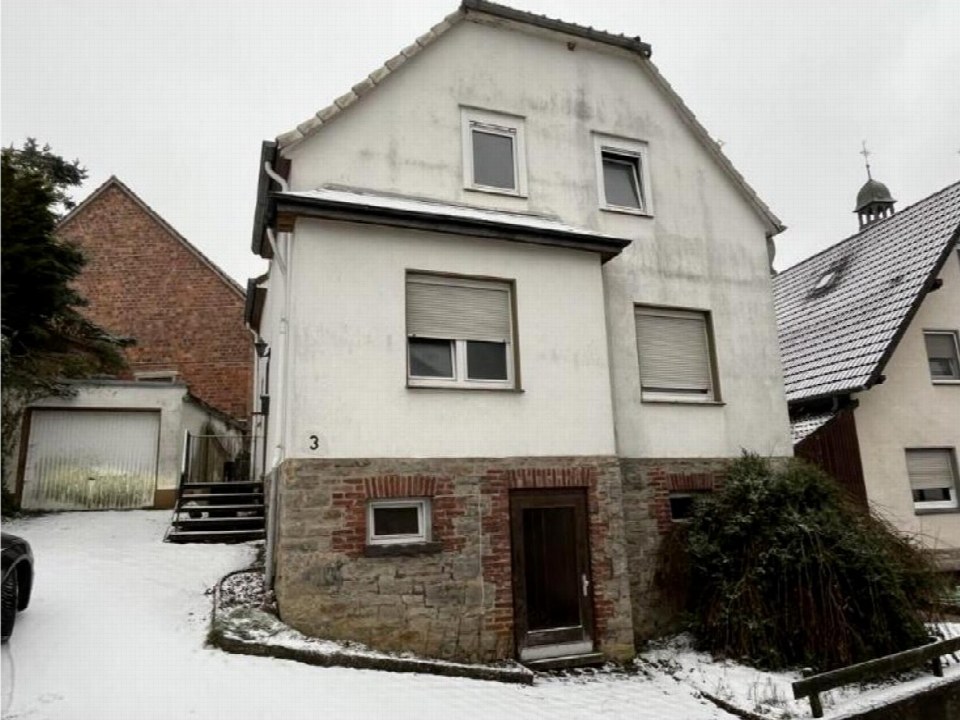Einfamilienhaus in Marsberg, Aschenstr. 3, mit weißer Fassade, Steinsockel und verschneitem Vorgarten. Eingangstür und Fenster sichtbar