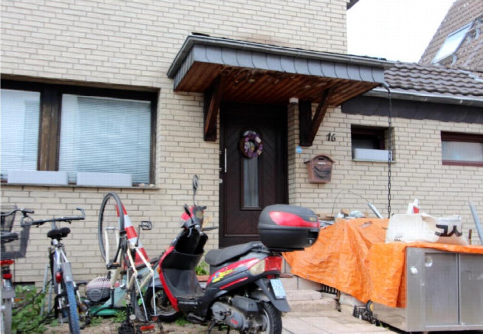 Eingangsbereich eines Reihenhauses mit dunkler Tür, Hausnummer 16, Vordach und geparktem Roller sowie Fahrrädern vor der Fassade