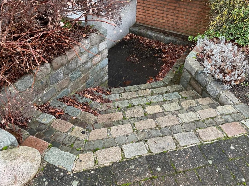 Steinplattenweg mit Stufen zum Eingang eines Gebäudes, umgeben von Mauern und Pflanzen