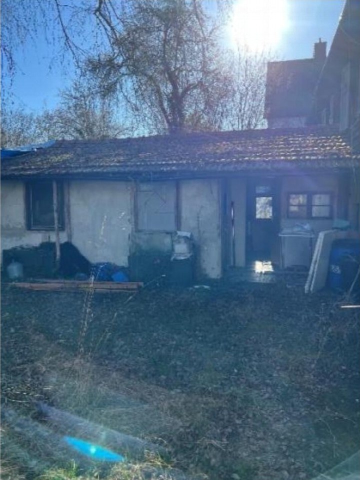 Rückansicht eines Einfamilienhauses mit Ziegeldach, Fenstern, Tür und unordentlichem Gartenbereich mit Laub und Gegenständen