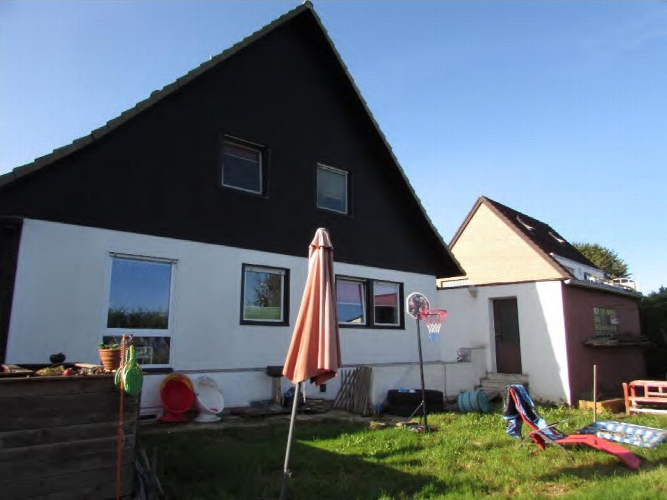 Hinterhof eines Einfamilienhauses mit Rasen, Sonnenschirm, Liegestuhl und Basketballkorb