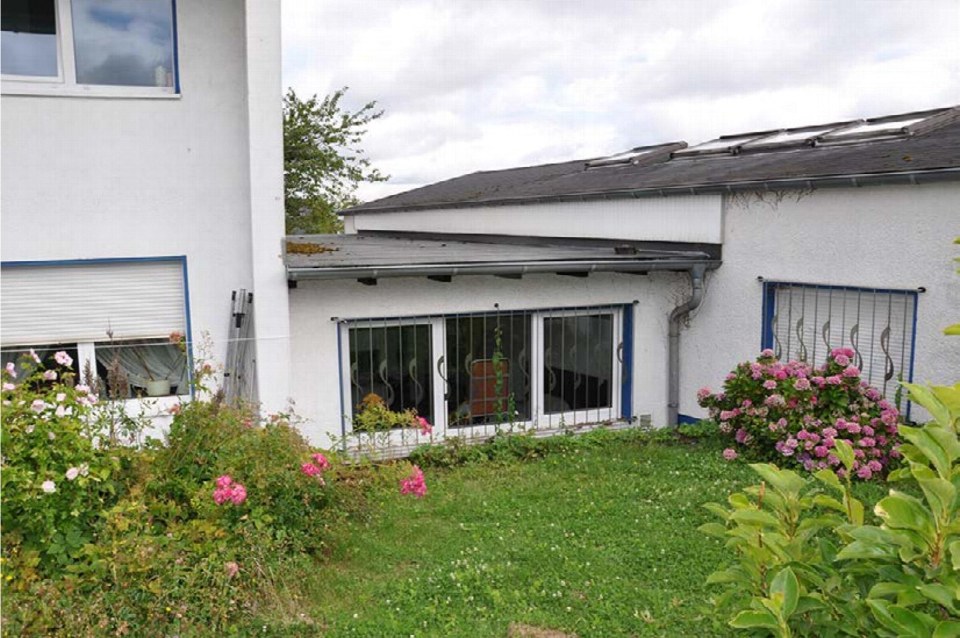 Gartenbereich mit grünem Rasen und blühenden Sträuchern vor einem weißen Einfamilienhaus mit Fenstern und Dachüberstand
