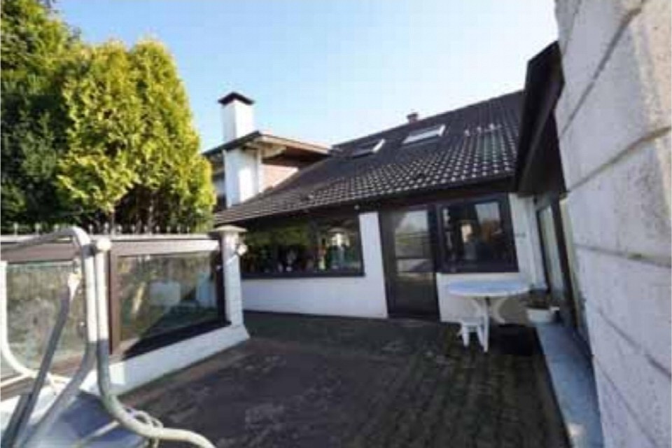 Terrasse eines Einfamilienhauses mit Pflasterbelag, weißer Tisch und Stühlen, großflächigen Fenstern und Dachgauben im Hintergrund