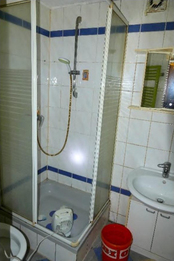 Badezimmer mit Dusche, Waschbecken, Toilette und Fliesenwand mit blauen Akzentstreifen