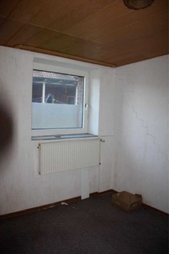 Leerer Raum mit Fenster, Heizkörper, Holzdecke und dunklem Bodenbelag im Einfamilienhaus Deichstraße 21, 46419 Isselburg Dieses