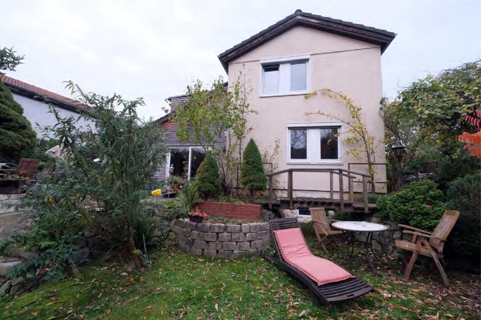 Hintergarten eines Einfamilienhauses mit Rasen, Pflanzen, Steinmauer, Liegestuhl und Holzterrasse
