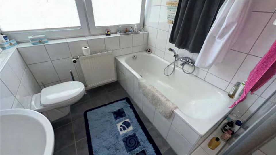 Badezimmer mit Badewanne, Toilette, Waschbecken, Fliesenwand und Fenster im Mehrfamilienhaus in Dinslaken