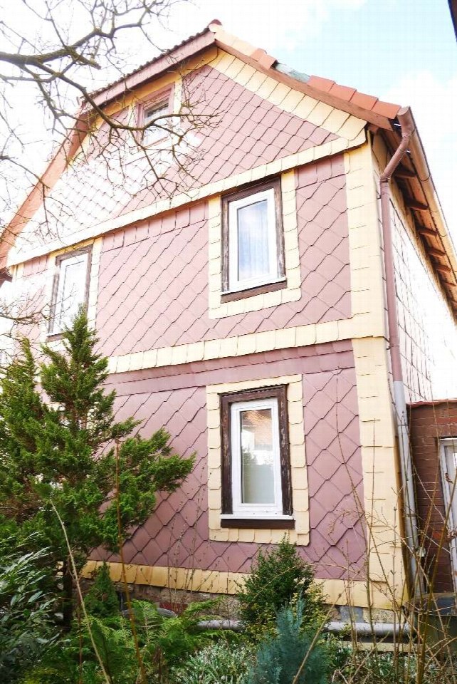 Seitenansicht eines Gebäudes mit rosa Schindelverkleidung, Fenstern und Dach, umgeben von Grünanlagen in Bernterode