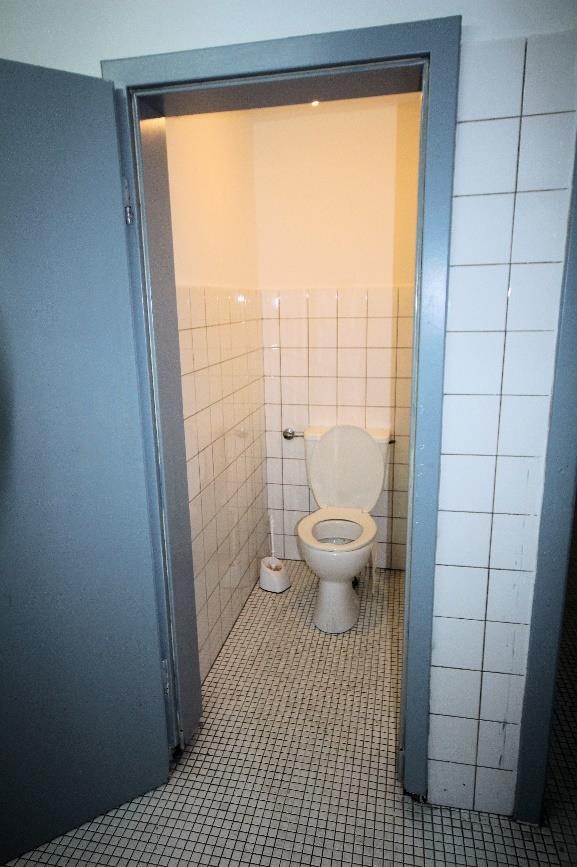 Kleiner Badezimmerbereich mit Toilette, weißen Fliesenwänden und gefliestem Boden, grauer Türumrandung, Teil einer Gewerbeeinheit in Dorsten
