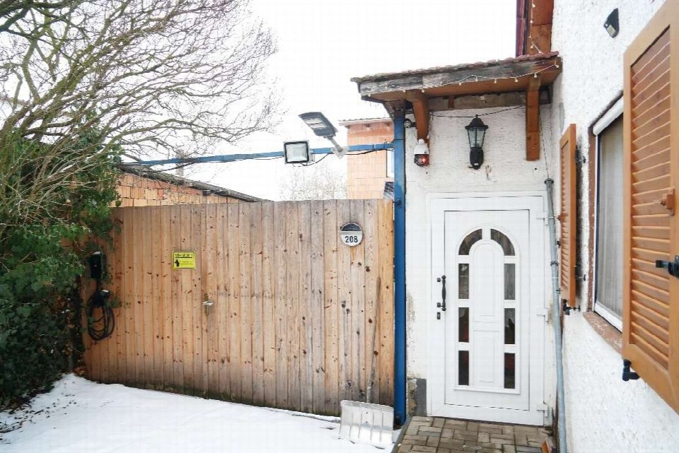 Eingangsbereich eines Hauses mit weißer Tür, Holzveranda und Zaun, Hausnummer 208, Schnee am Boden