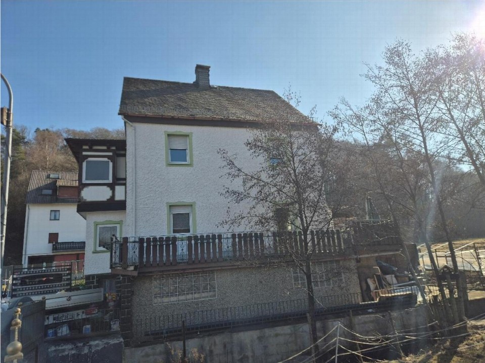 Seitenansicht eines mehrstöckigen Wohnhauses mit Balkon und Fenstern, umgeben von Bäumen, in Spitzboden, Waldstraße 4