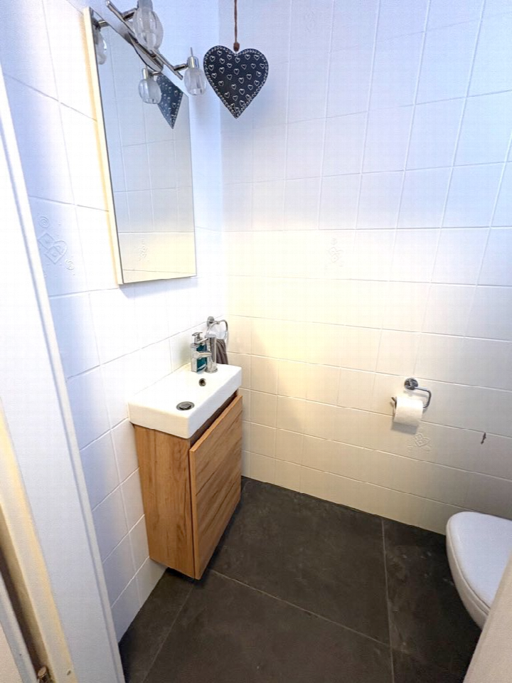 Badezimmer mit weiß gefliesten Wänden, Holzwaschtisch, Spiegel und Toilettenpapierhalter