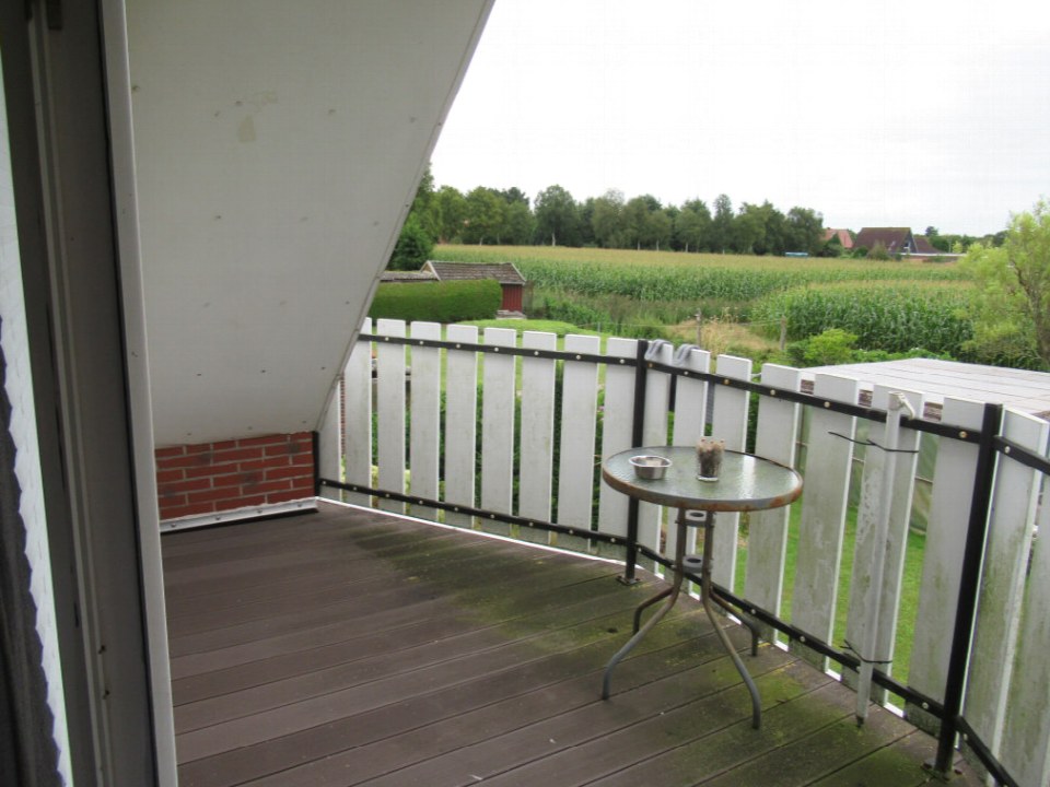 Holzbalkon mit weißer Brüstung und kleinem Tisch, Blick auf Feld und Bäume