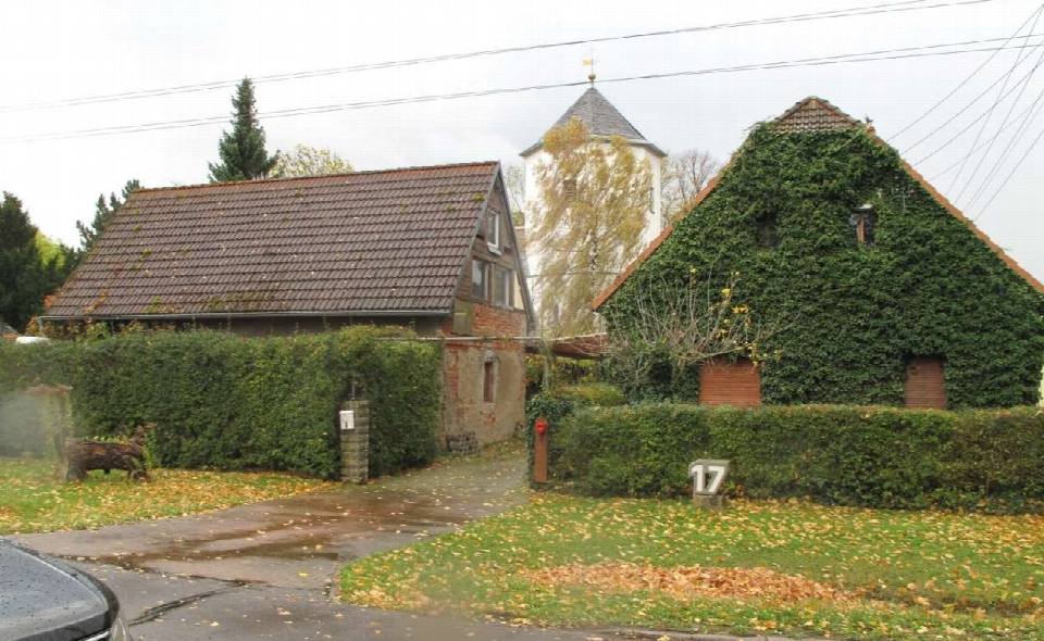 Vorderansicht eines Grundstücks mit Haus Nr. 17, umgeben von Hecken und weiteren Gebäuden, im Herbst mit Laub auf dem Boden