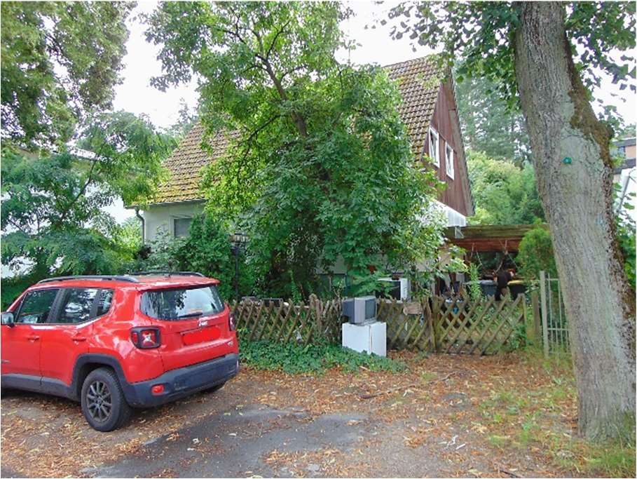 Rotes SUV vor einem Haus mit Garten und Holzzaun