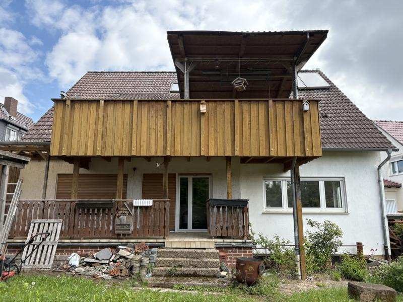 Vorderansicht eines Einfamilienhauses mit Holzbalkon, Eingangstür und Vorgarten in Felsberg, Vorderbinge 11
