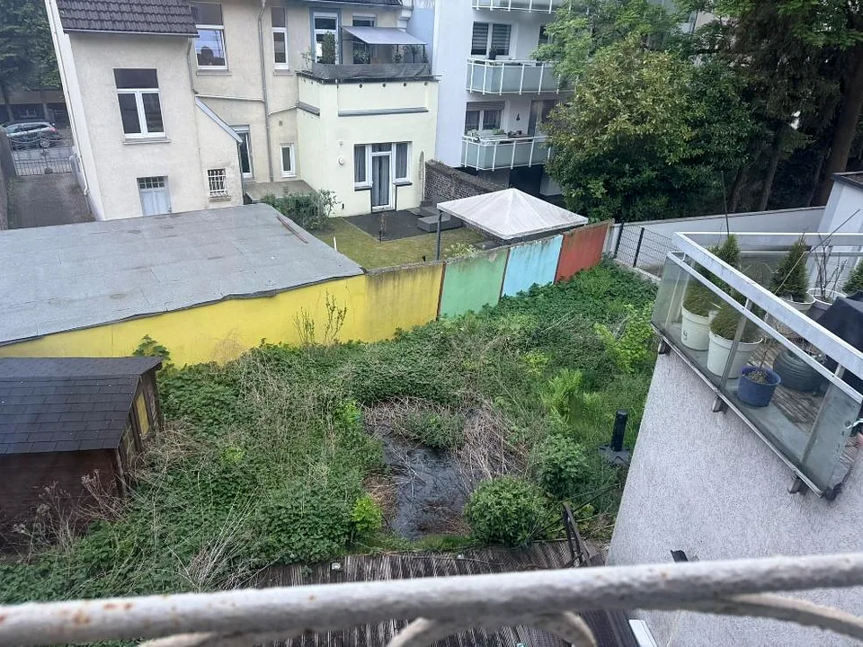 Überwuchertes Grundstück mit buntem Zaun und angrenzenden Gebäuden in Essen, Germaniastraße 241