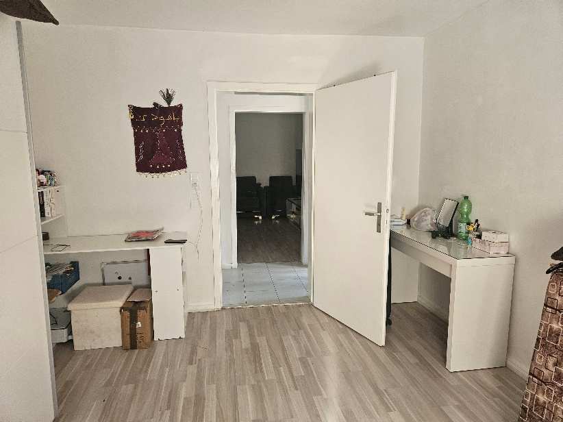 Innenraum eines Einfamilienhauses in Augsburg, Flurstraße 25, mit Holzdielenboden, weißer Tür, Schreibtisch und Regal. Im Hintergrund weitere Räume sichtbar