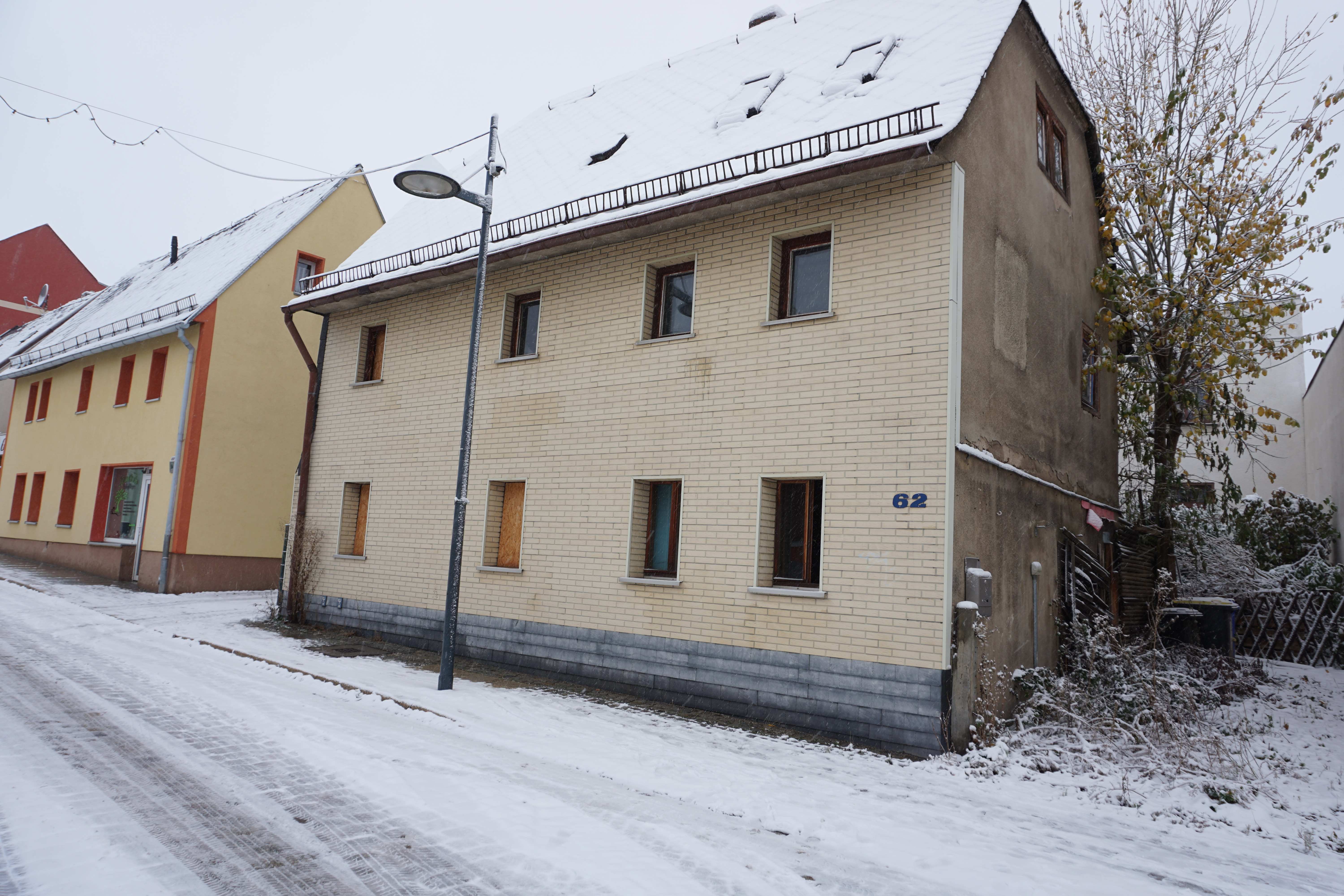 Seitenansicht eines zweistöckigen Gebäudes mit verschneitem Dach und Fenstern, Hausnummer 62, in einer verschneiten Straße