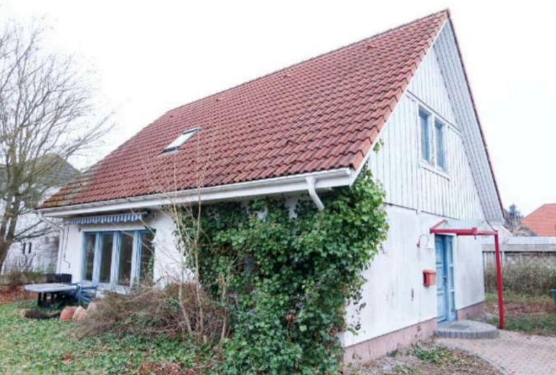 Einfamilienhaus in Trassenheide, Birkenweg 6, mit rotem Ziegeldach, weißer Fassade und Efeubewuchs an der Seite. Vordere Ansicht mit blauer Tür und Fenstern