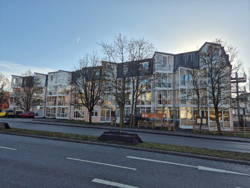 Fassade eines mehrstöckigen Gebäudes in Ansbach, Ludwig-Keller-Str. 40, mit Glasfassaden und Balkonen, umgeben von kahlen Bäumen und Straße