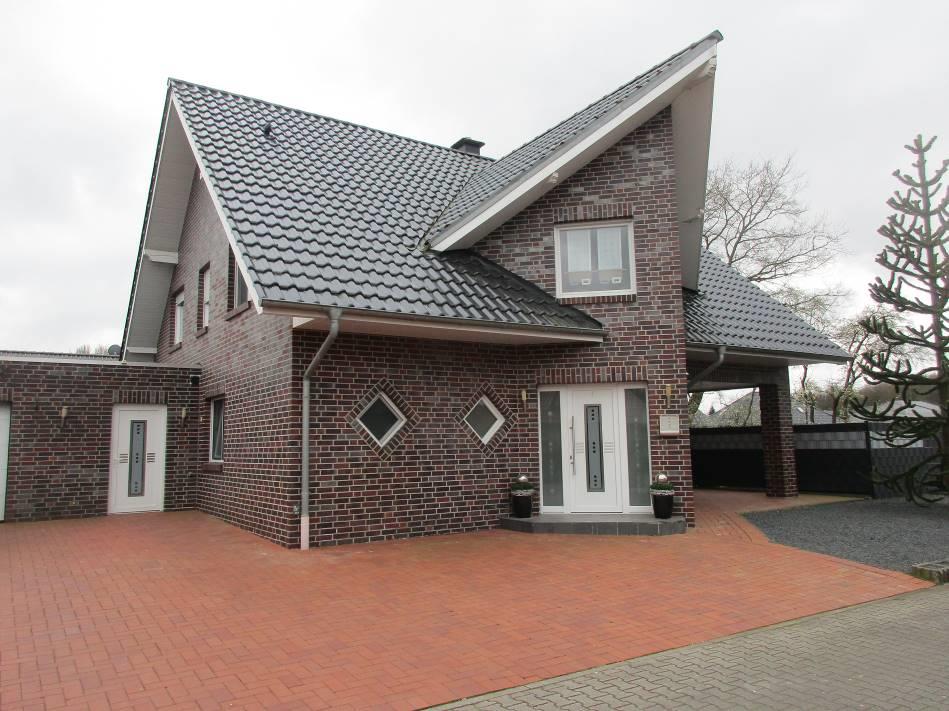 Einfamilienhaus in Werlte, 49757, mit rotem Ziegelmauerwerk, dunklem Wellblechdach, zwei Eingangstüren und rotem Pflasterhof vorne