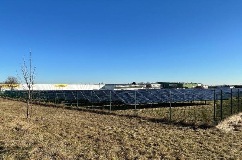 Solaranlage auf einem Feld in Emersleben, Bruchweg, 38822, unter klarem blauen Himmel, umgeben von einem Zaun, im Hintergrund Gebäude